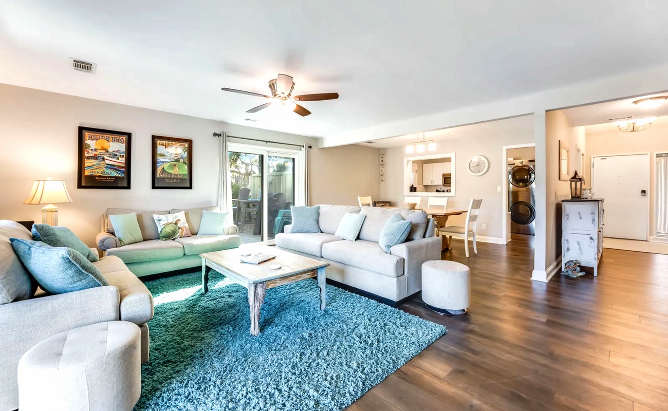 Sink into plush sofas in your bright, open living space where teal accents and warm wood floors create the perfect atmosphere for relaxing.