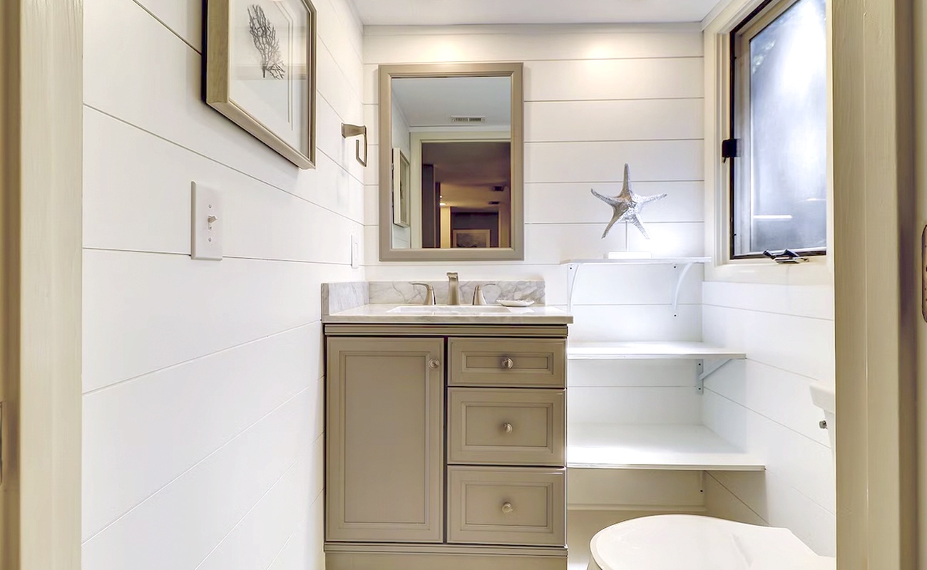 Step into your beautifully appointed bathroom with marble countertops, coastal-inspired decor, and crisp white shiplap walls that create a serene spa-like retreat.