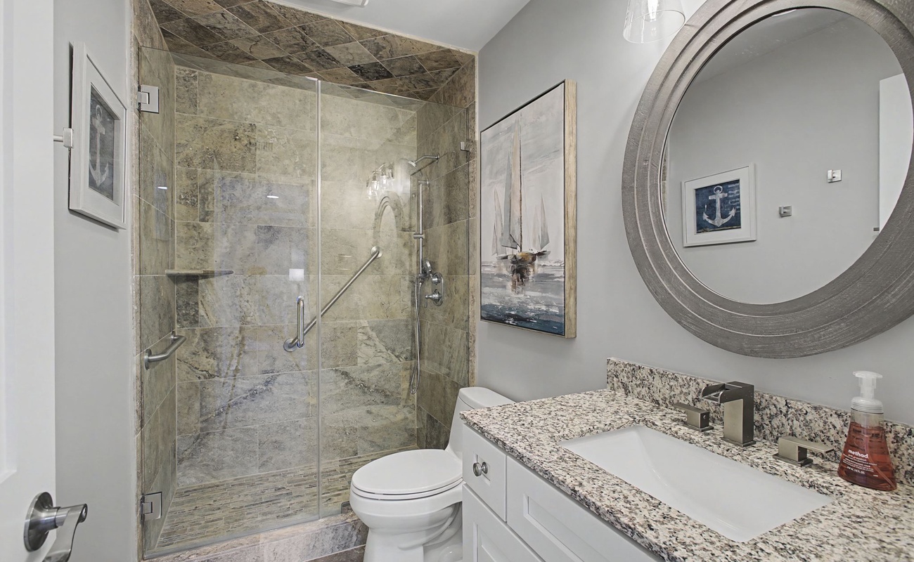 Step into your beautifully appointed bathroom featuring a luxurious stone-tiled shower, granite countertops, and elegant coastal decor that makes your daily routine feel like a spa retreat.