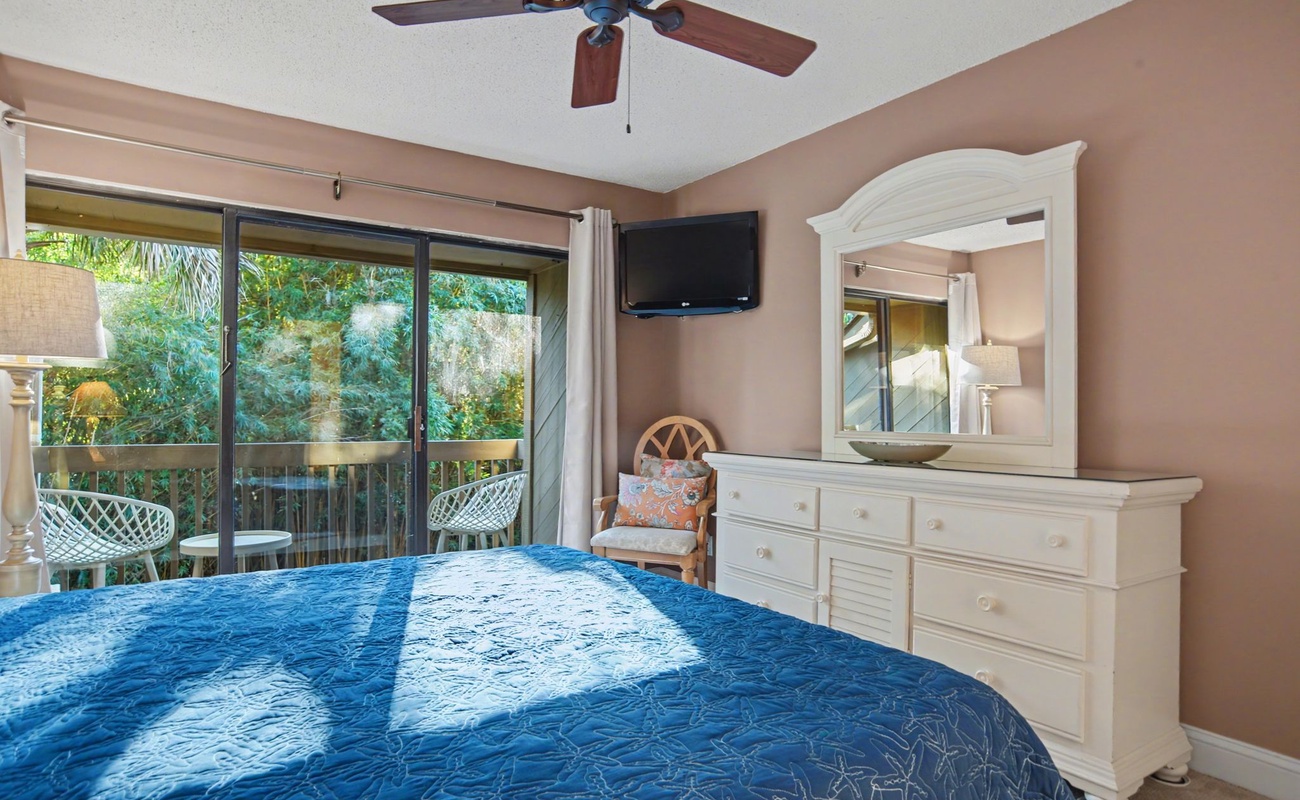 Relax in your peaceful bedroom with garden views through sliding doors, complete with ceiling fan and cozy seating nook.
