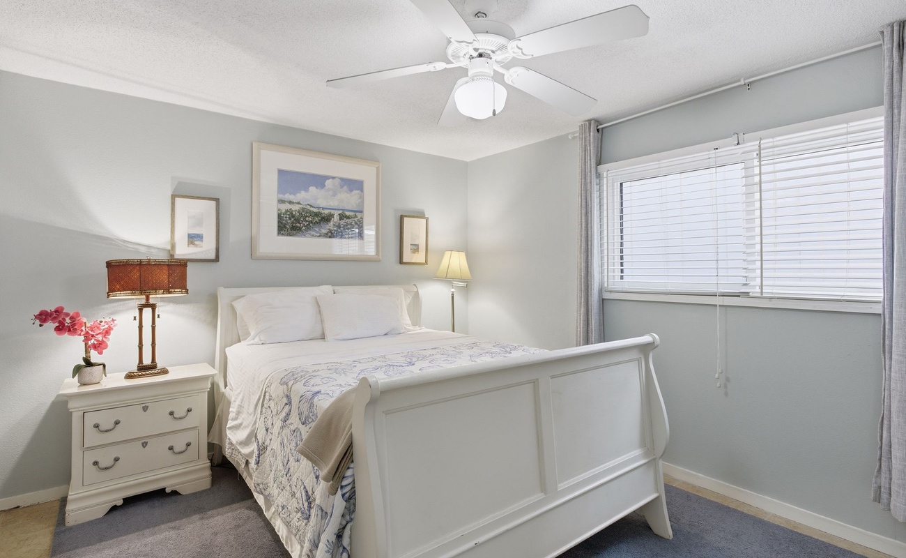 Rest peacefully in your serene bedroom featuring a comfortable white sleigh bed, ceiling fan for perfect temperature, and soft natural light filtering through blinds.