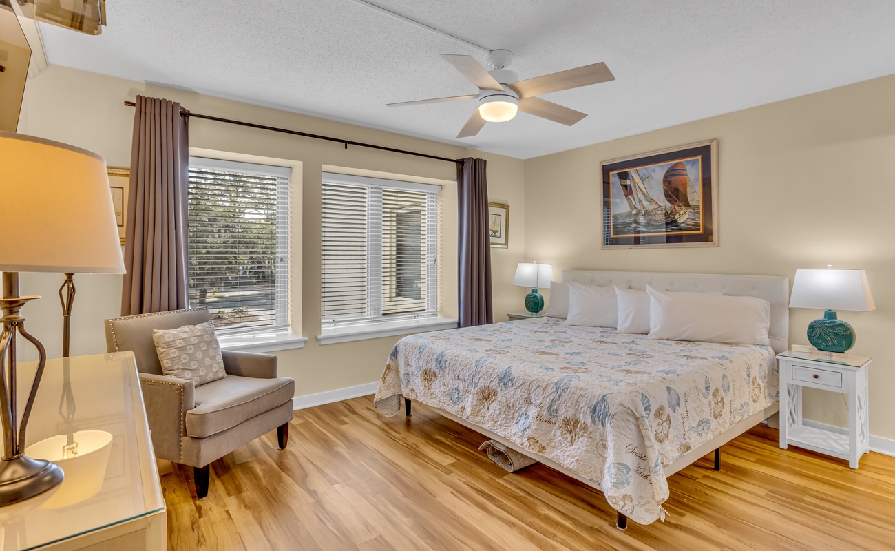 Unwind in your serene bedroom featuring polished hardwood floors, a comfortable reading chair, and gentle natural light filtering through the windows.