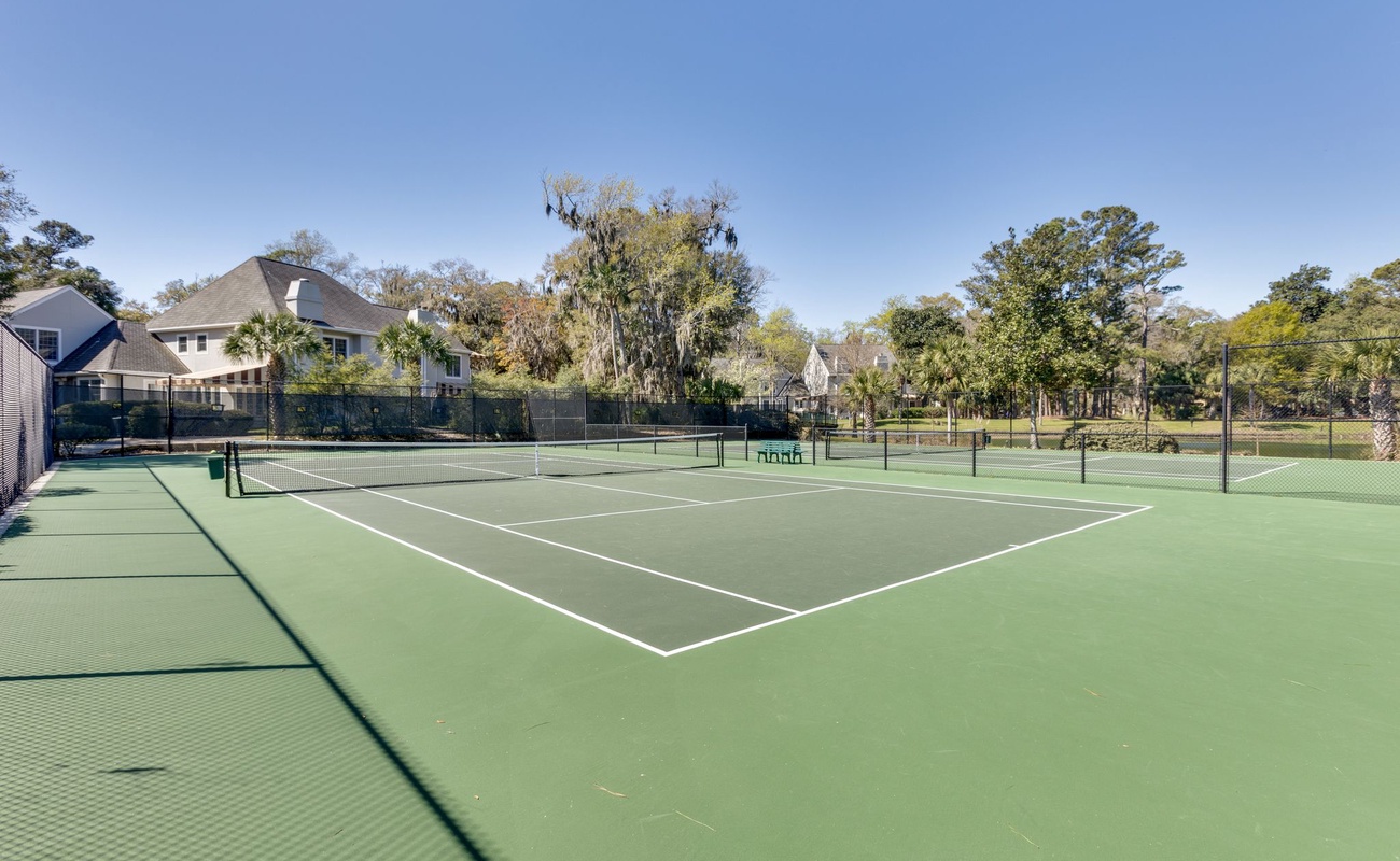 Professional tennis courts nestled in a peaceful residential setting with mature trees and blue skies overhead.