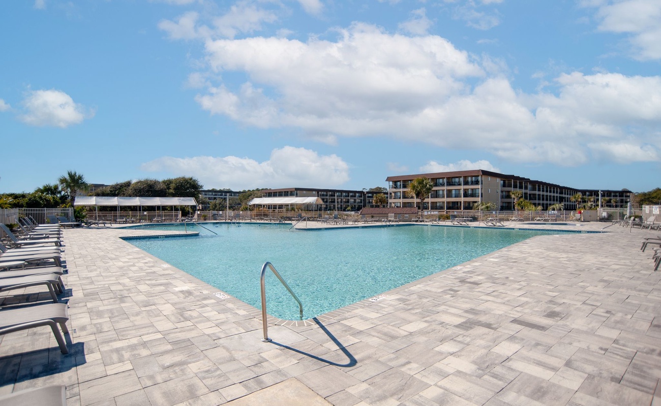 Large resort-style swimming pool with expansive deck and multi-story buildings in a tropical coastal setting.