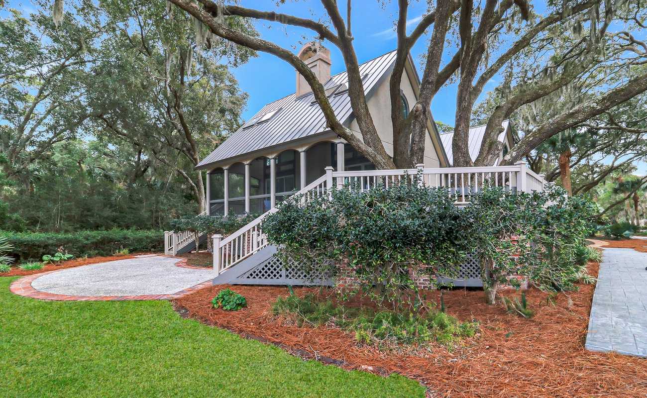 Charming property nestled among mature trees with wraparound porch and beautifully landscaped grounds featuring manicured lawn and garden beds.