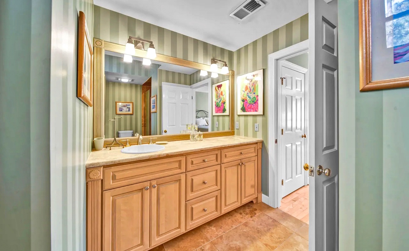 Refresh in your elegant bathroom featuring warm wood vanity, marble countertops, and charming floral artwork for a delightful morning routine.