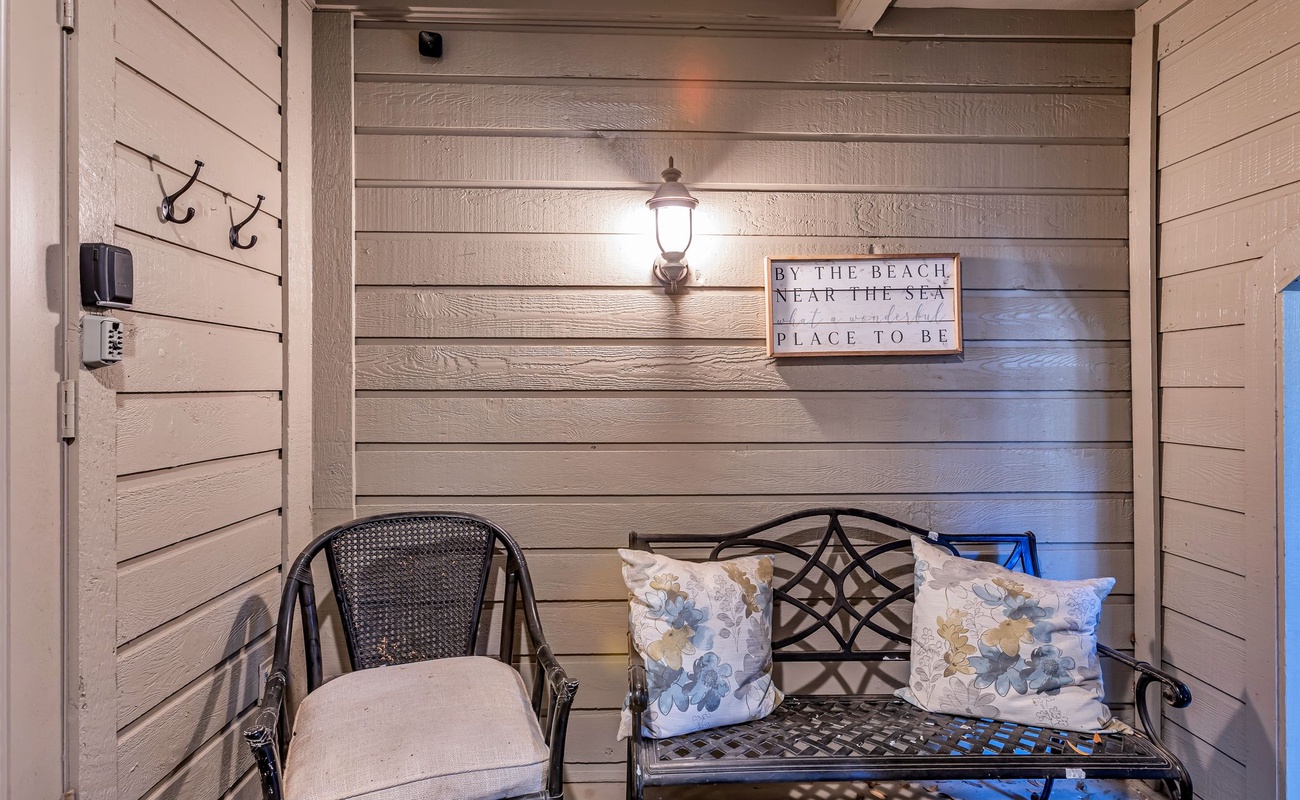 Unwind on your private covered patio with cozy seating, coastal charm, and soft evening lighting creating the perfect retreat.