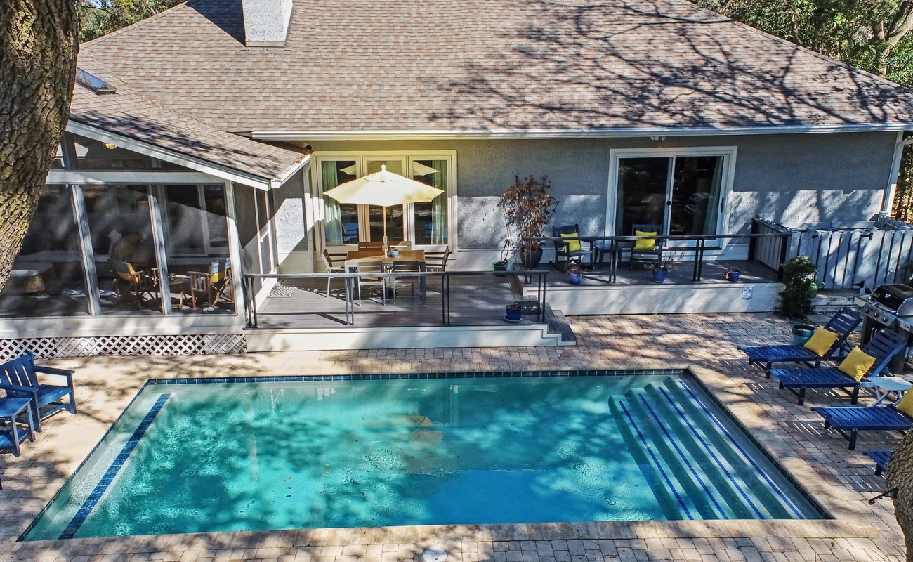 Beautiful vacation home featuring a private swimming pool, spacious deck with outdoor dining, and screened porch surrounded by mature trees.