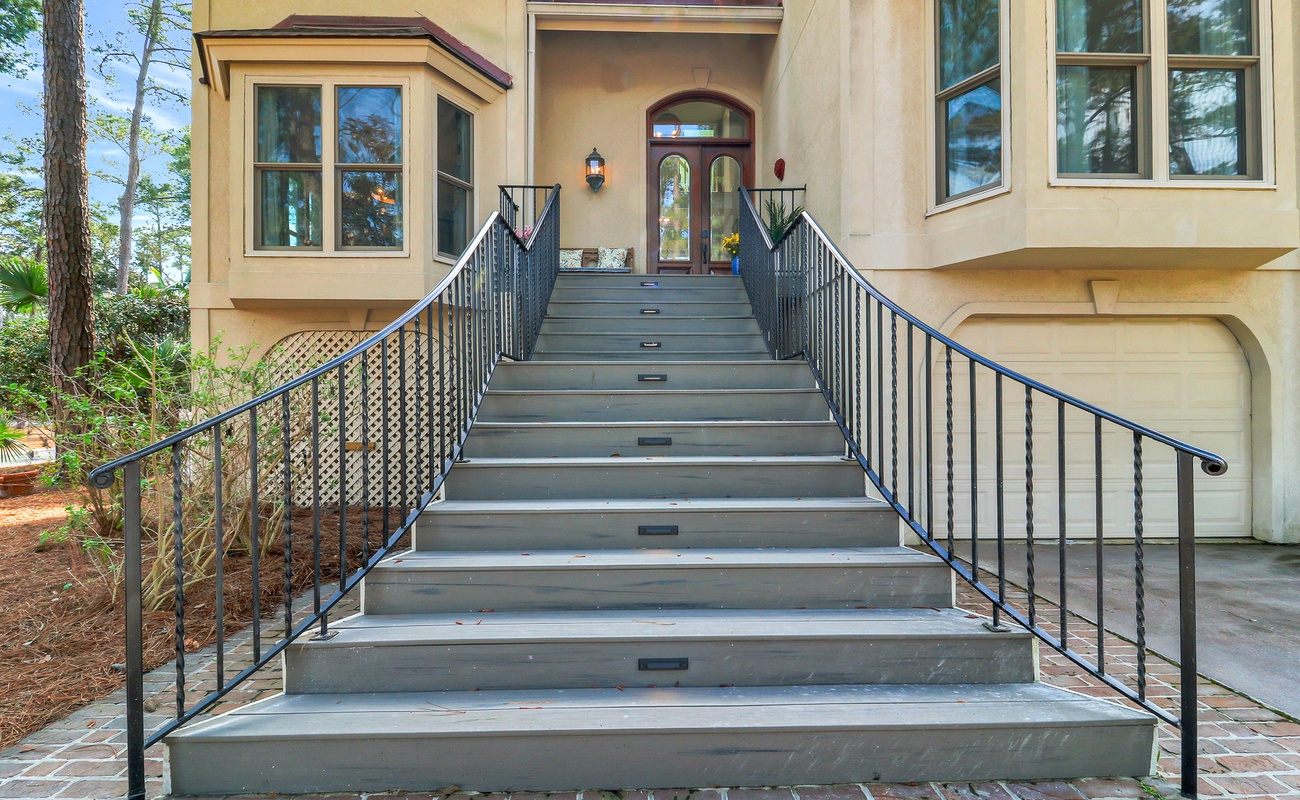 Elegant staircase leads to your welcoming front entrance, surrounded by mature trees and thoughtful landscaping.
