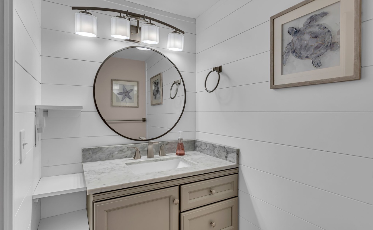 Refresh in your elegantly appointed bathroom featuring marble countertops, coastal artwork, and warm lighting that creates a serene spa-like atmosphere.