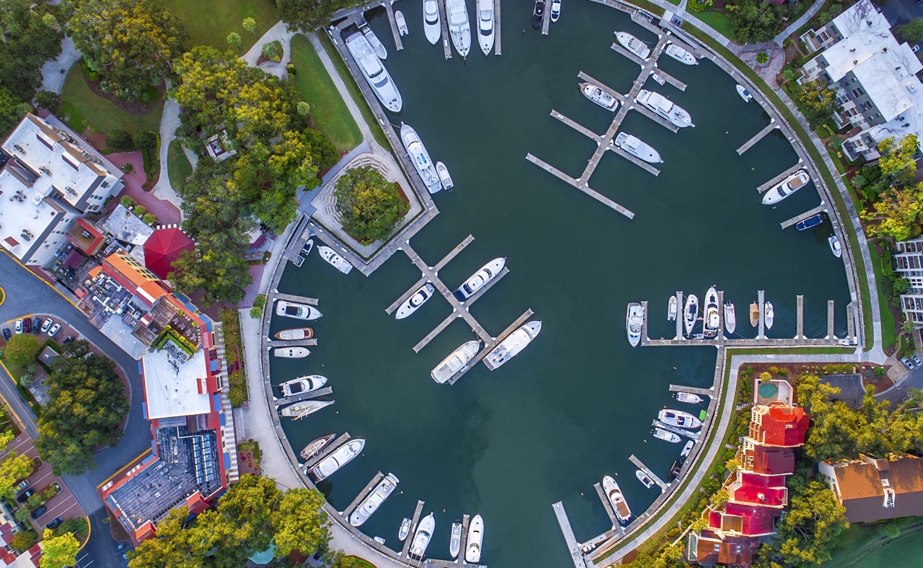 Aerial view of a circular marina filled with boats, surrounded by colorful buildings and tree-lined streets in the neighborhood.