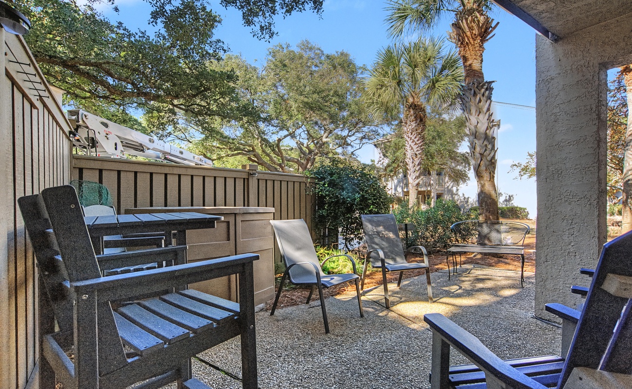 Your private covered patio features comfortable seating surrounded by lush landscaping and mature palm trees.