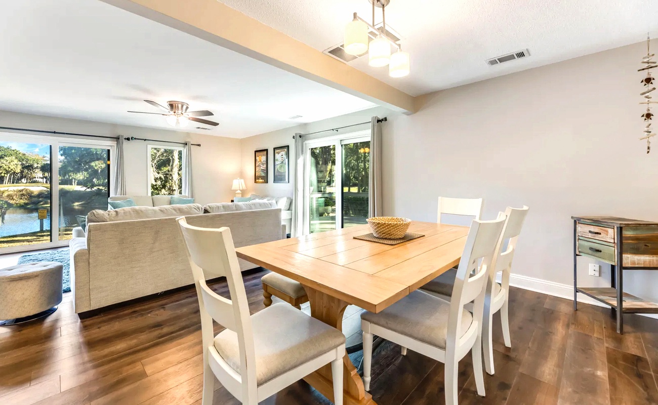 Your open-plan dining and living space features warm hardwood floors and large windows overlooking lush greenery, creating a bright and welcoming atmosphere for meals and relaxation.