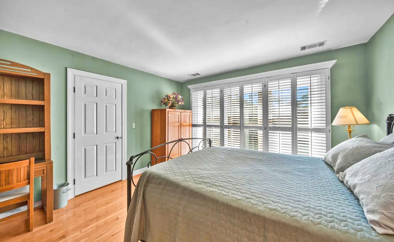 Drift off peacefully in your serene bedroom featuring soothing mint walls, elegant plantation shutters, and warm hardwood floors that create the perfect retreat.