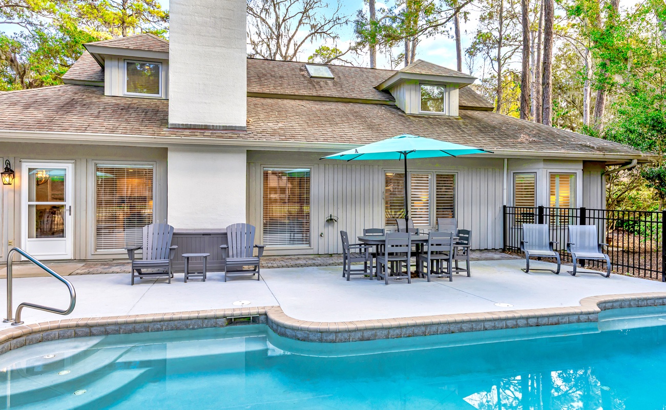 Your private oasis awaits with a sparkling pool, spacious patio dining, and comfortable loungers under swaying trees.