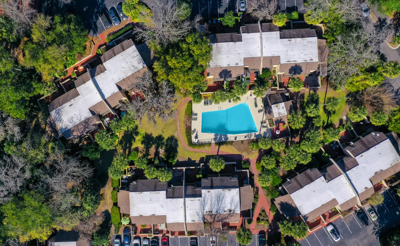Aerial view of the property nestled in a leafy residential area with multiple buildings surrounding a central swimming pool and landscaped grounds.