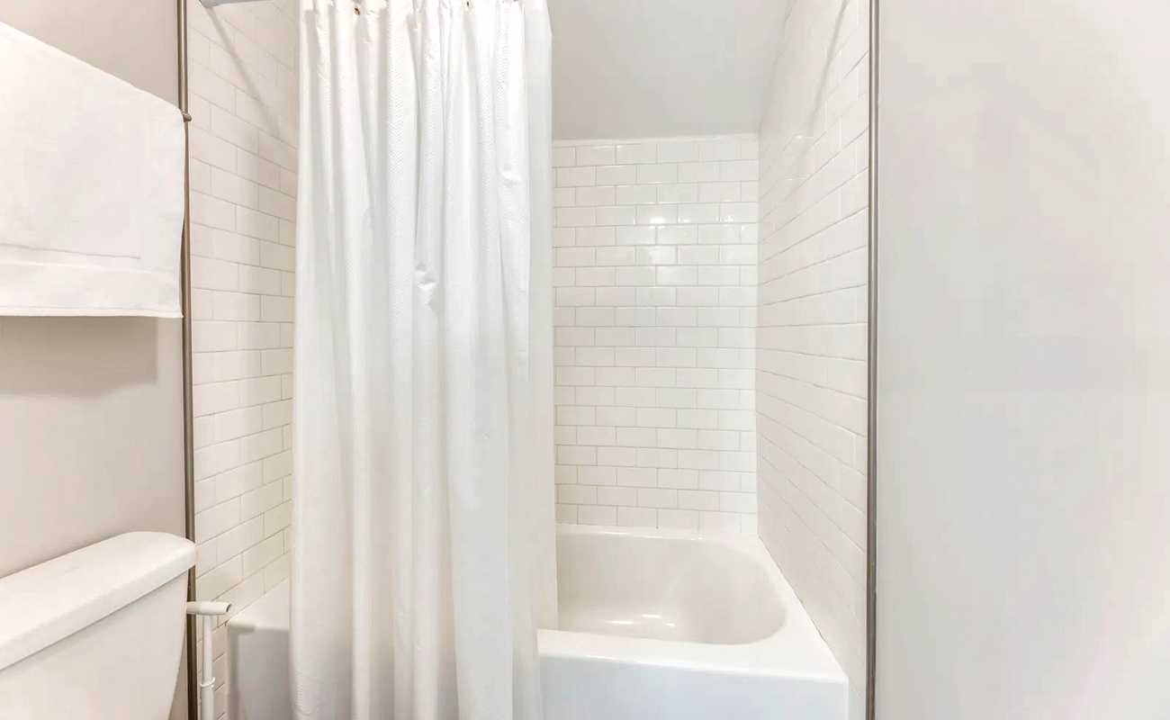 Refresh in your pristine bathroom featuring a gleaming tub-shower combo with classic subway tiles and crisp white curtains.