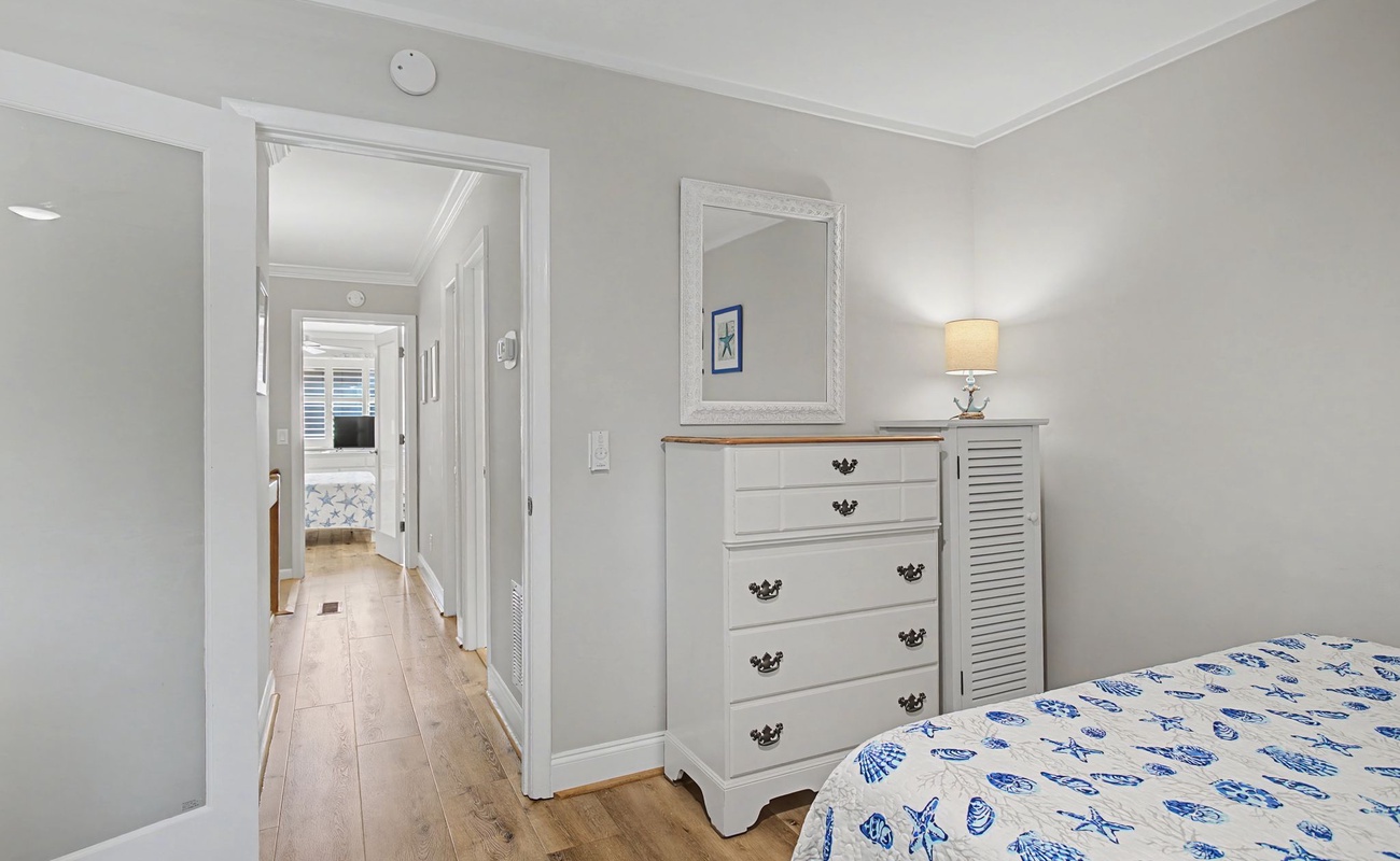 Your serene bedroom features elegant coastal-themed linens and a charming white dresser for storing your belongings.