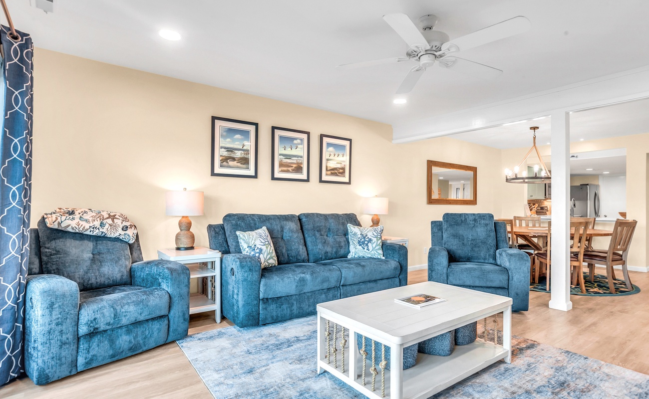 Settle into your spacious living room with plush blue seating and coastal artwork, perfect for relaxing after beach adventures.