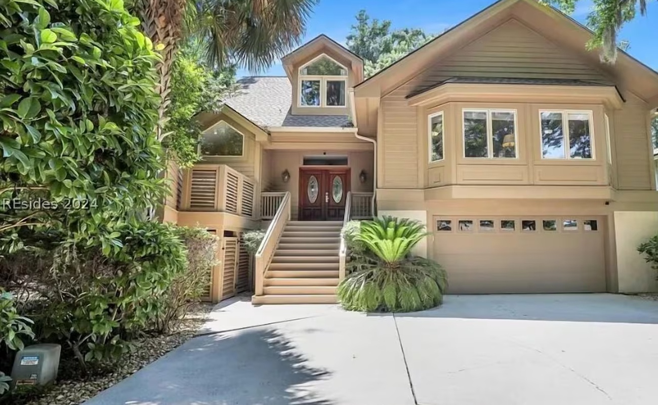 A welcoming coastal home featuring warm wood exterior, red front doors, and tropical landscaping with convenient parking.