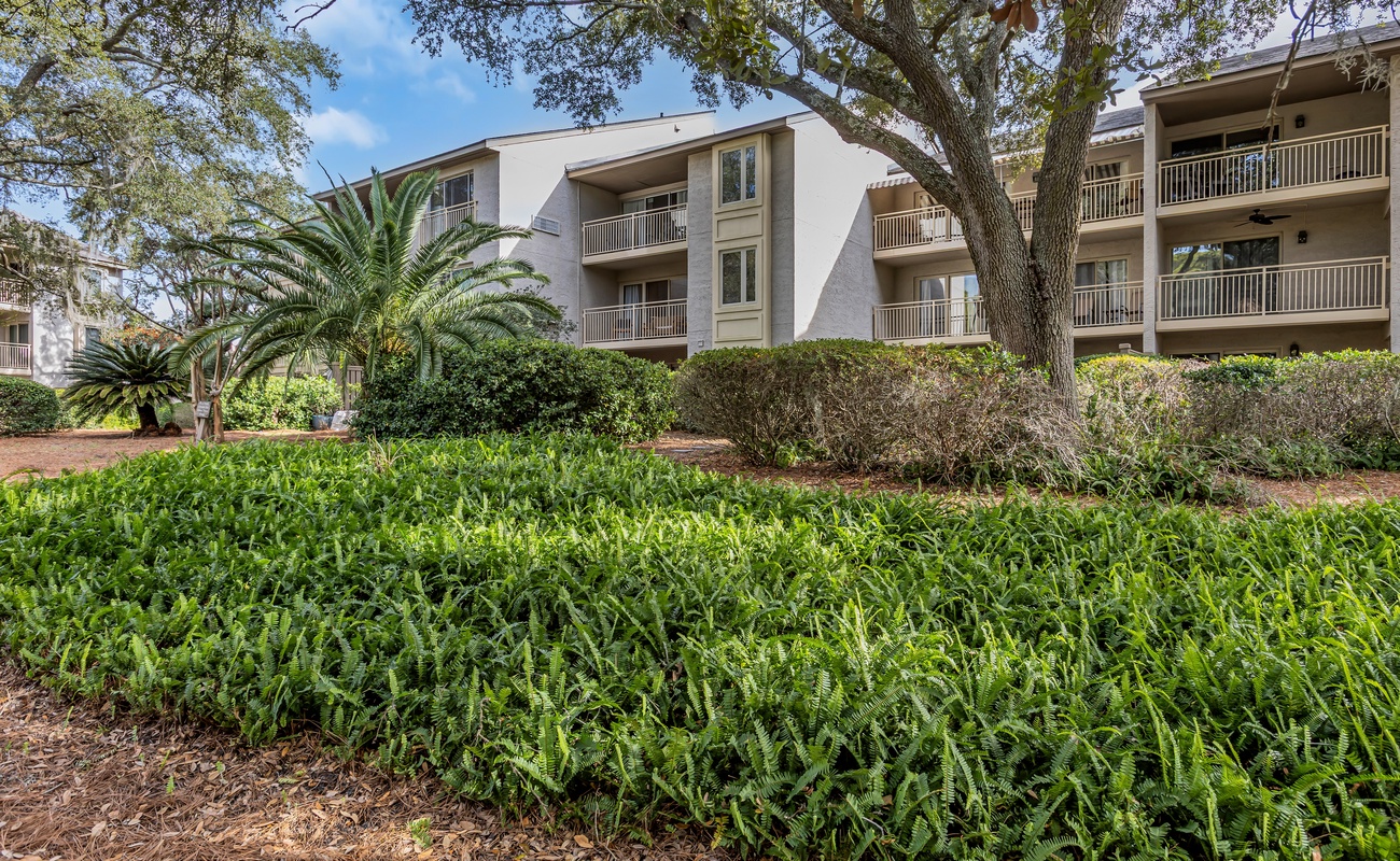 Multi-level property building surrounded by lush tropical landscaping and mature trees in a peaceful resort setting.