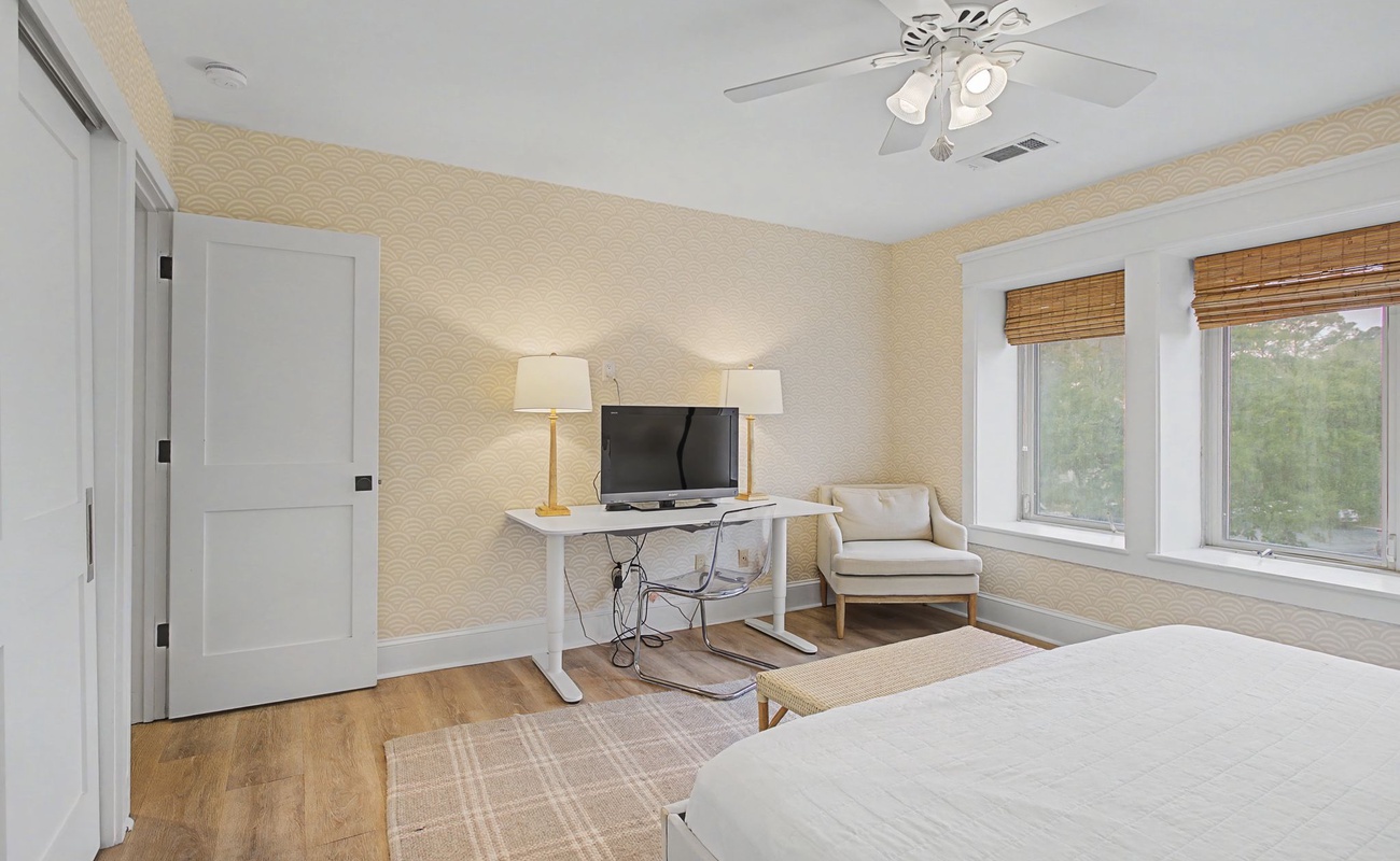 Unwind in your serene bedroom retreat with cozy seating, entertainment center, and peaceful garden views through bamboo shades.