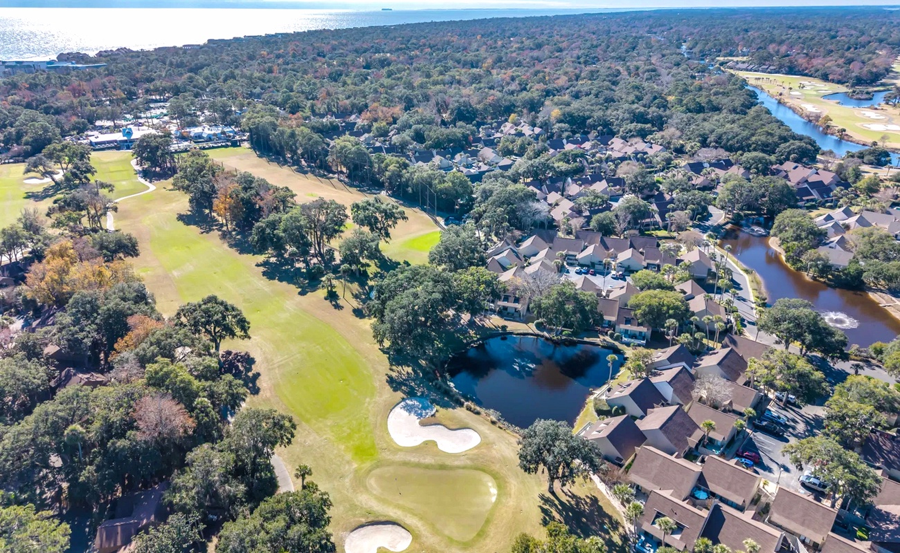 Aerial view of a coastal resort community featuring golf course fairways, waterways, and ocean access in a tree-lined setting.