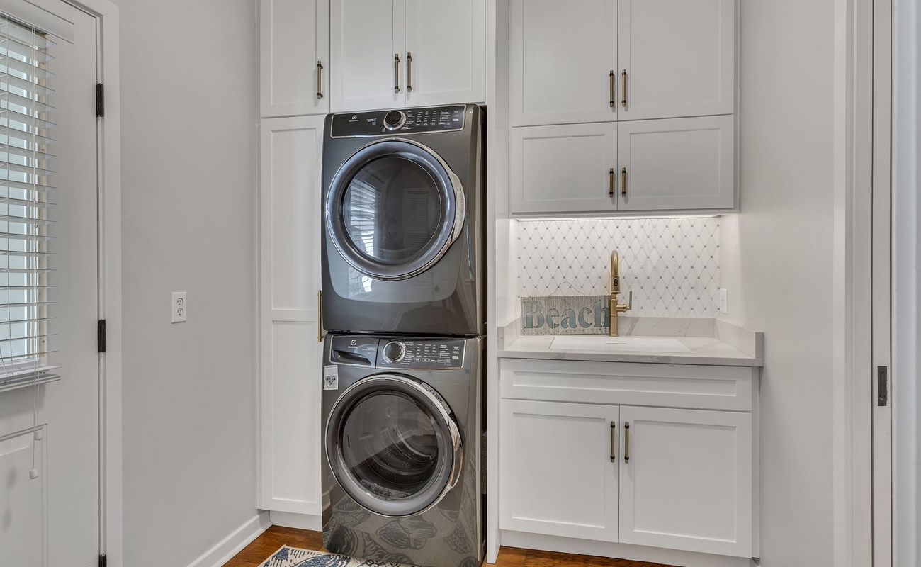 Your private laundry room features stacked washer and dryer, elegant white cabinetry, and a convenient utility sink for effortless care.