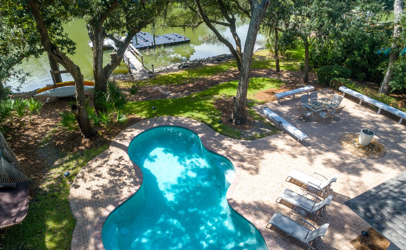 Aerial view shows the property's private pool area, dock access, and landscaped grounds with mature trees providing natural shade.