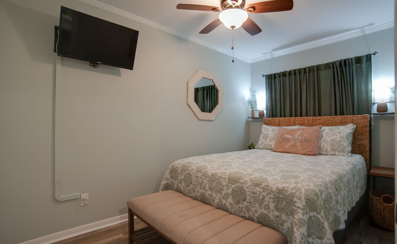 Drift off in your serene bedroom featuring a plush bed, calming decor, wall-mounted TV, and gentle ceiling fan for perfect comfort.