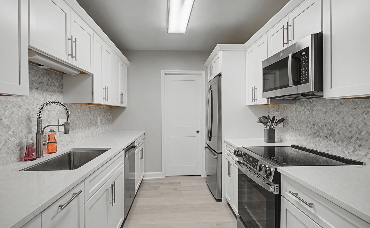 You'll love cooking in this pristine galley kitchen with sleek white cabinets, modern appliances, and elegant marble-pattern backsplash.