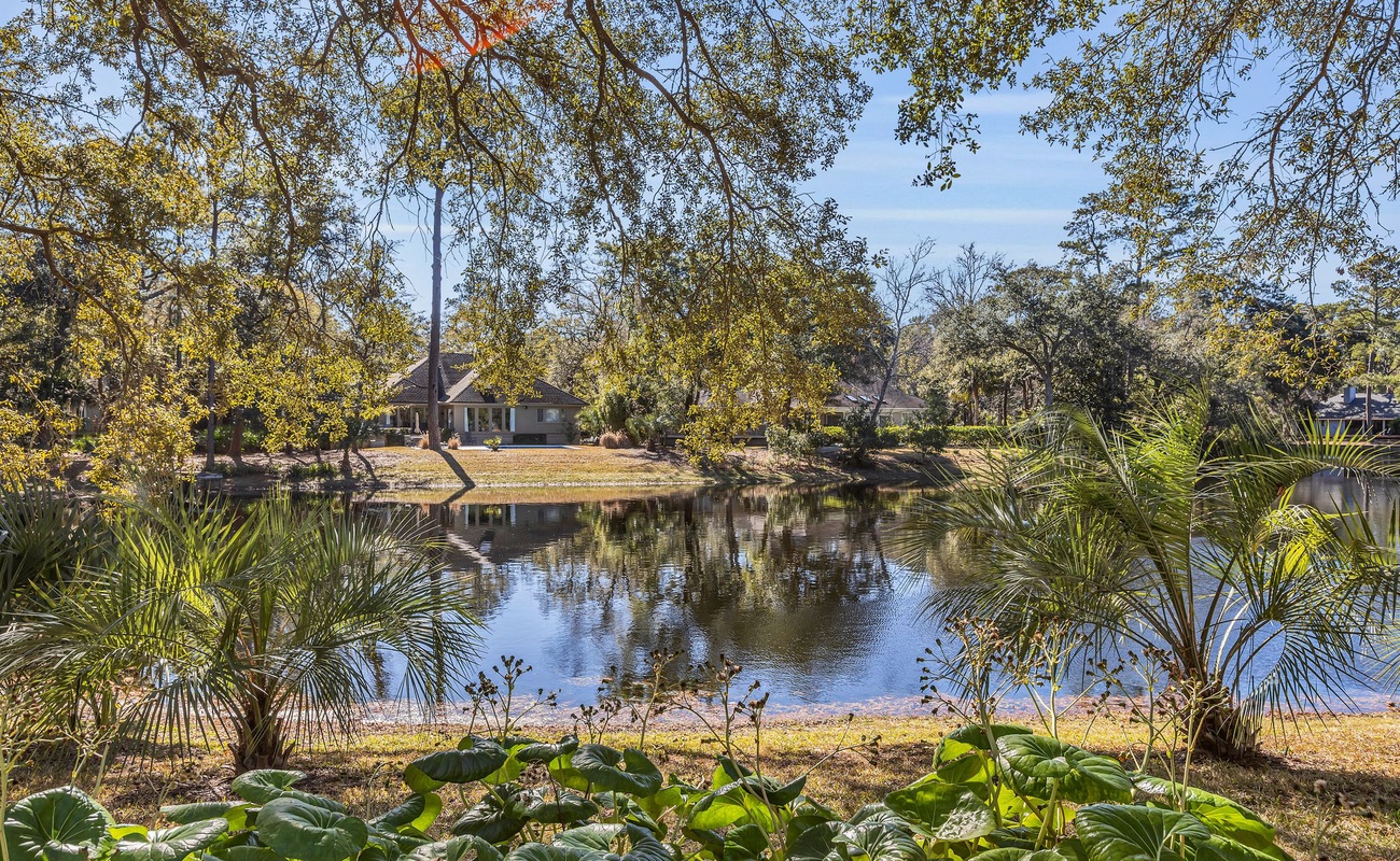 Peaceful lakefront property nestled among mature trees with tropical landscaping and tranquil water views.