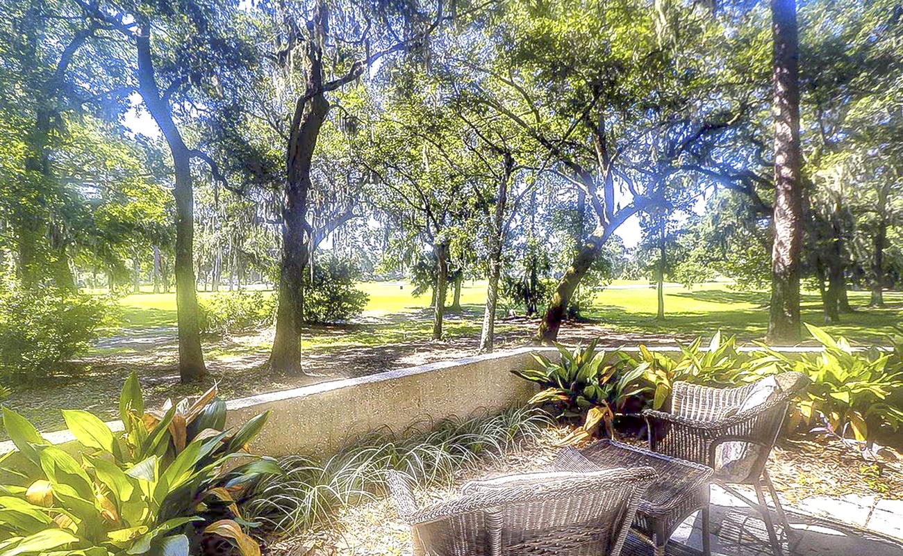 Your private patio overlooks lush gardens where tropical plants frame wicker seating under towering shade trees.