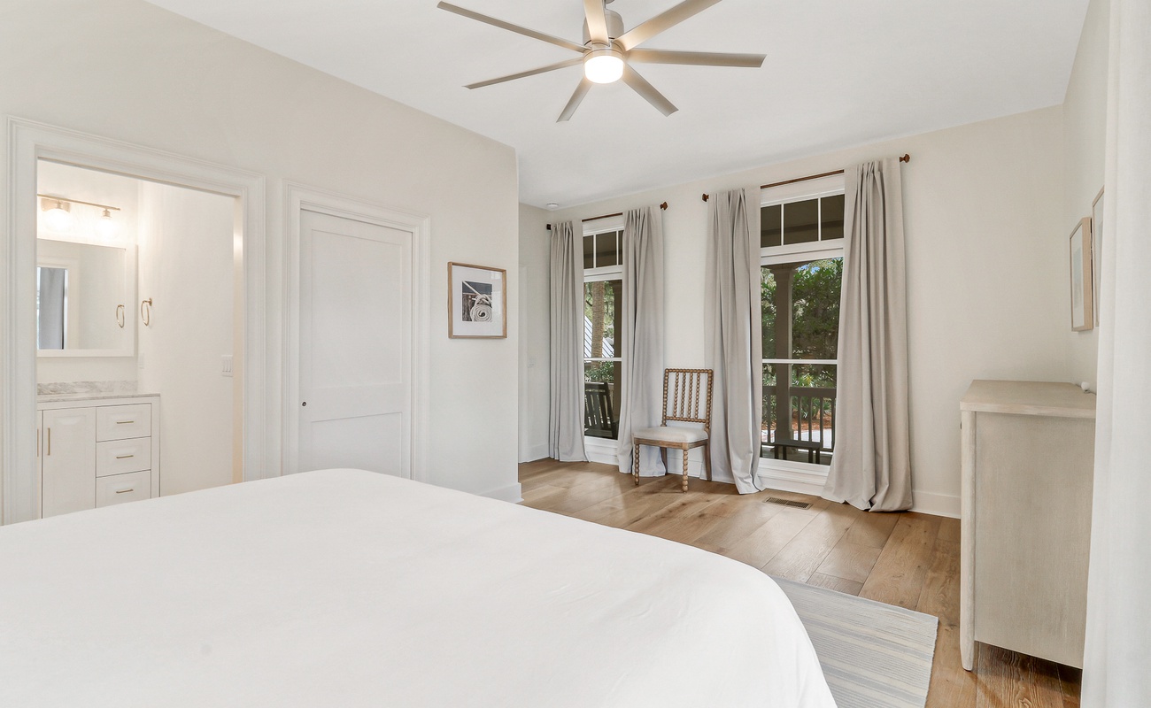 Drift off in your serene bedroom featuring crisp white linens, warm hardwood floors, and gentle natural light streaming through French doors to your private balcony.