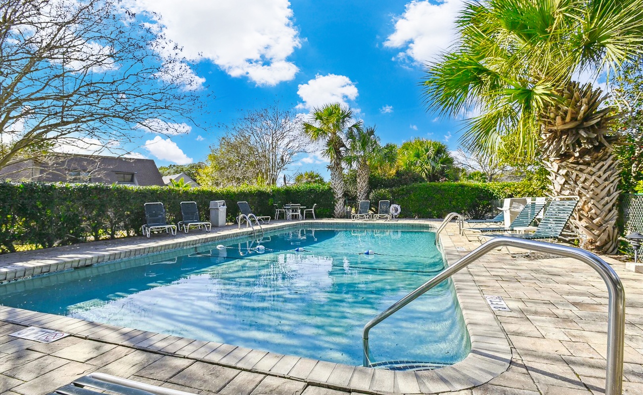 Dive into your private oasis with crystal-clear waters reflecting blue skies, surrounded by tropical palms and comfortable lounging spots for ultimate relaxation.