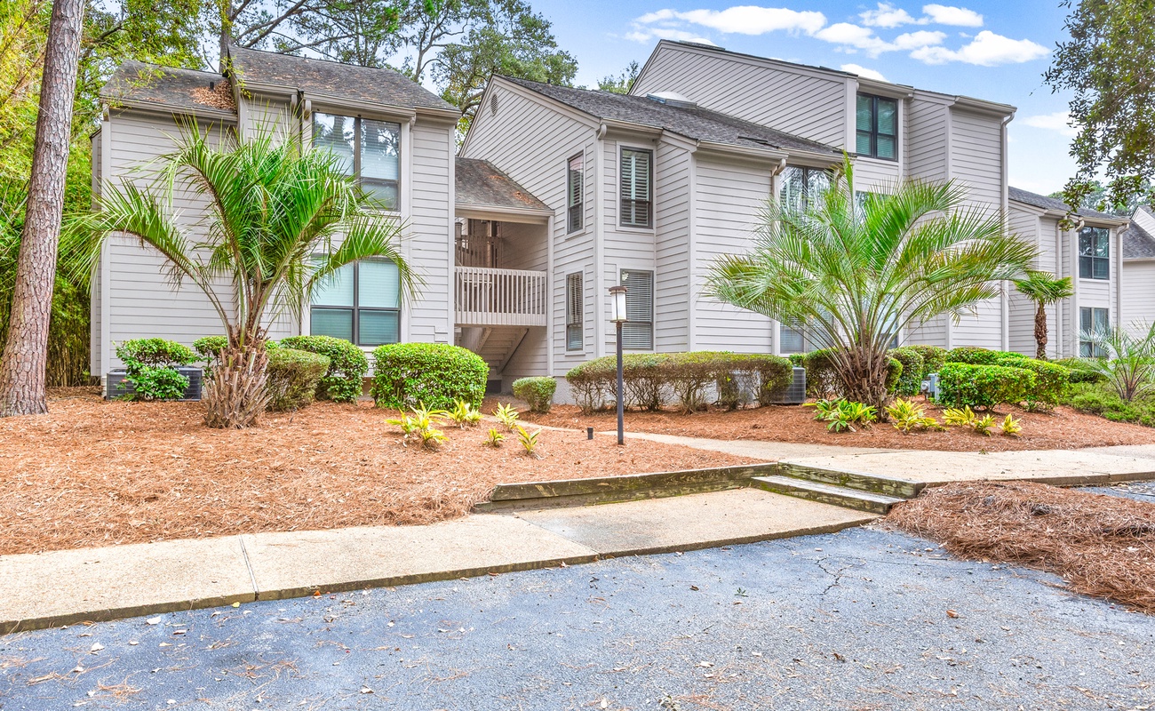 Modern residential buildings nestled among mature trees with tropical palm landscaping and well-maintained grounds.