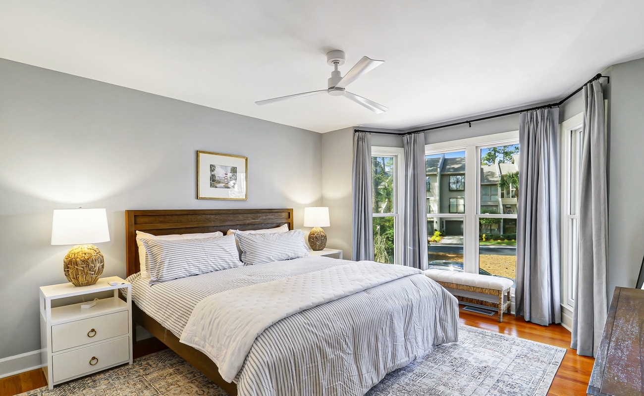 Drift off to sleep in your serene bedroom with crisp linens, gentle ceiling fan, and peaceful neighborhood views through floor-to-ceiling windows.