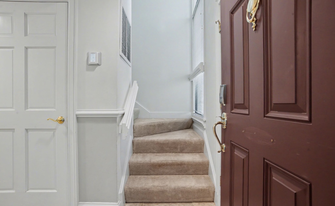 Step into your welcoming entrance where warm wood doors and soft carpeted stairs create an inviting atmosphere for your home away from home.