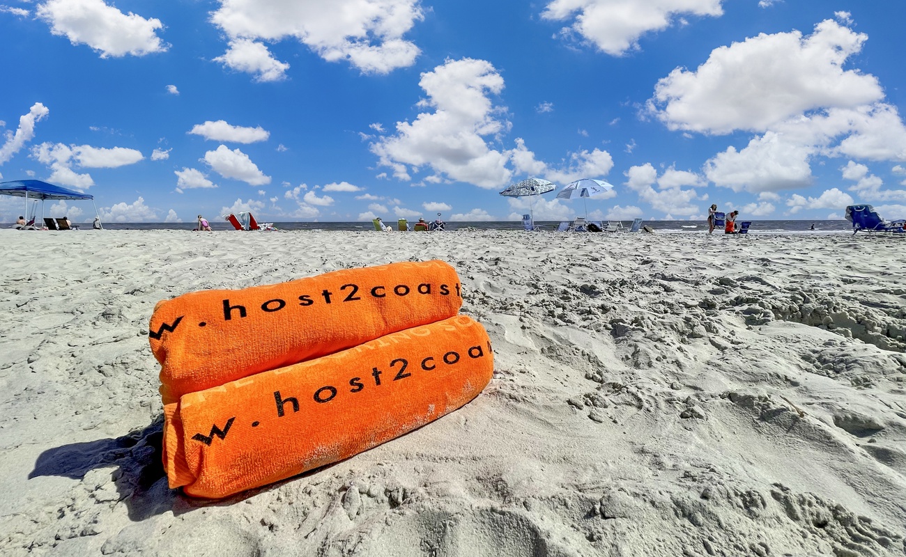 Branded beach towels mark this pristine stretch of sand with umbrellas and beachgoers enjoying the coastline.