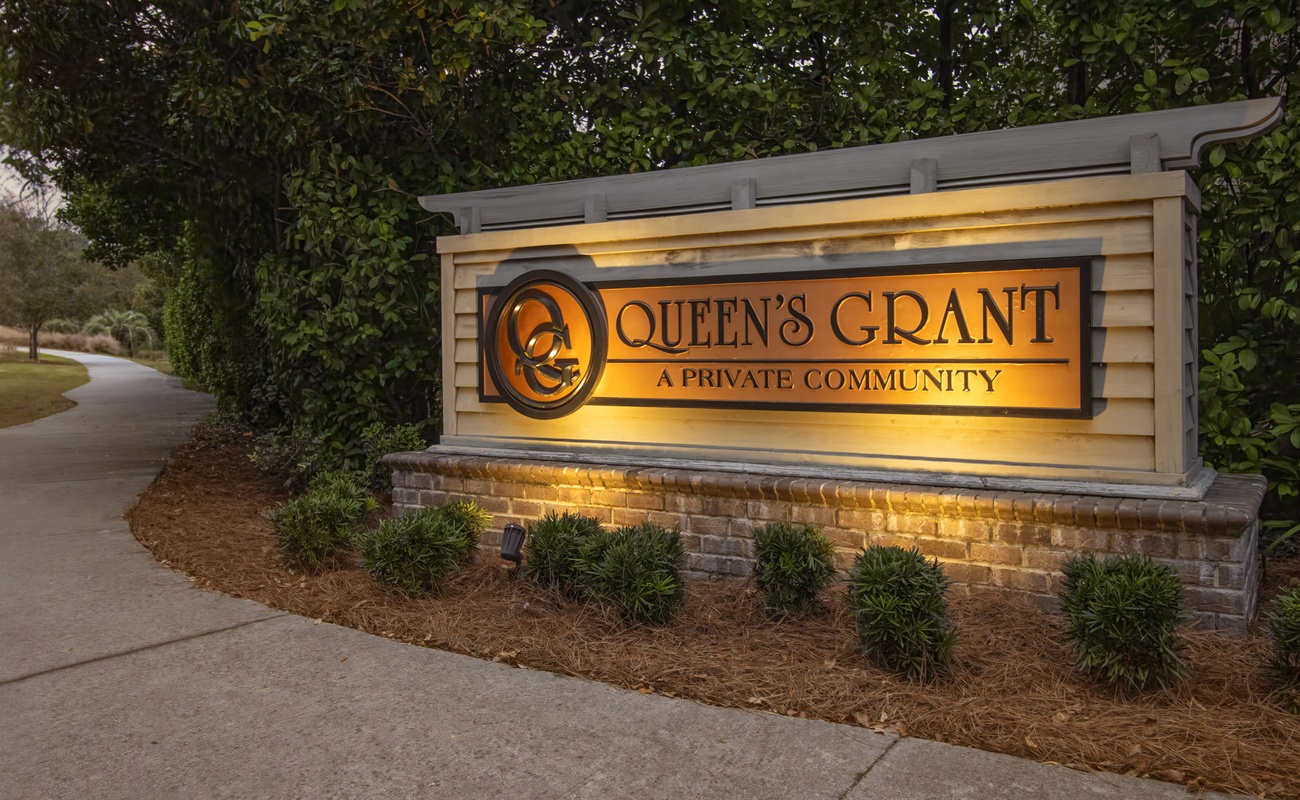 Illuminated entrance sign for Queen's Grant private community, featuring elegant landscaping and welcoming lighting for evening arrivals.