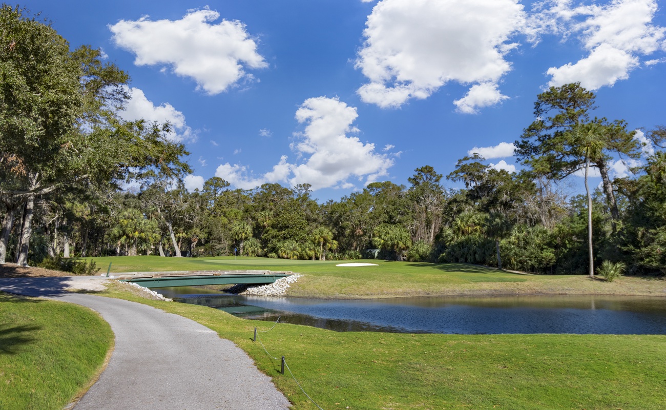 Beautiful golf course fairway with water hazard and walking path surrounded by lush Florida landscape.
