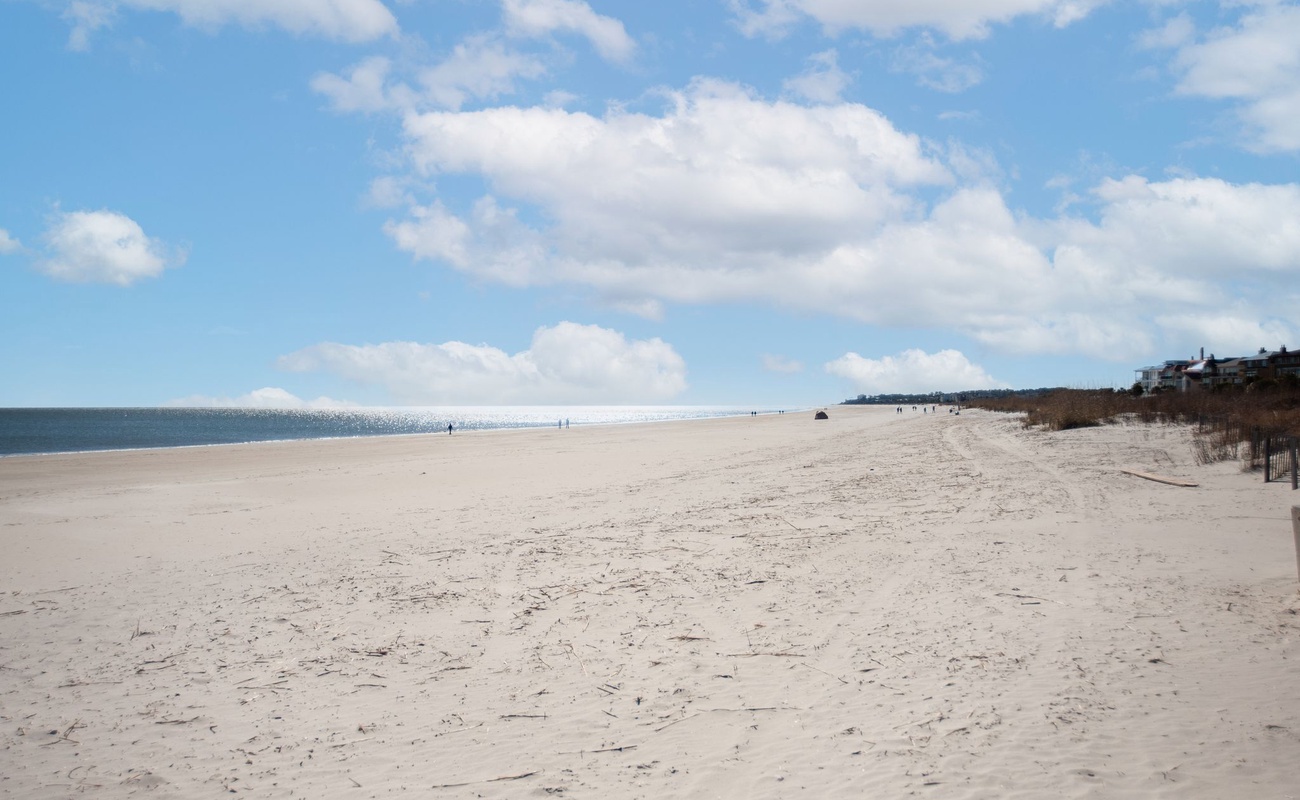 Expansive sandy beach stretches along the coastline with gentle waves and scattered beachgoers enjoying the pristine waterfront setting.