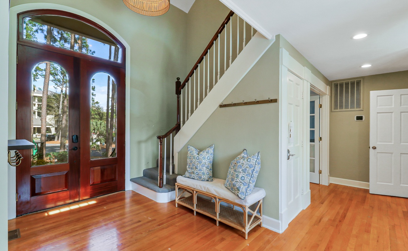 Step into your welcoming entryway where warm hardwood floors and elegant blue-patterned pillows create an inviting first impression.