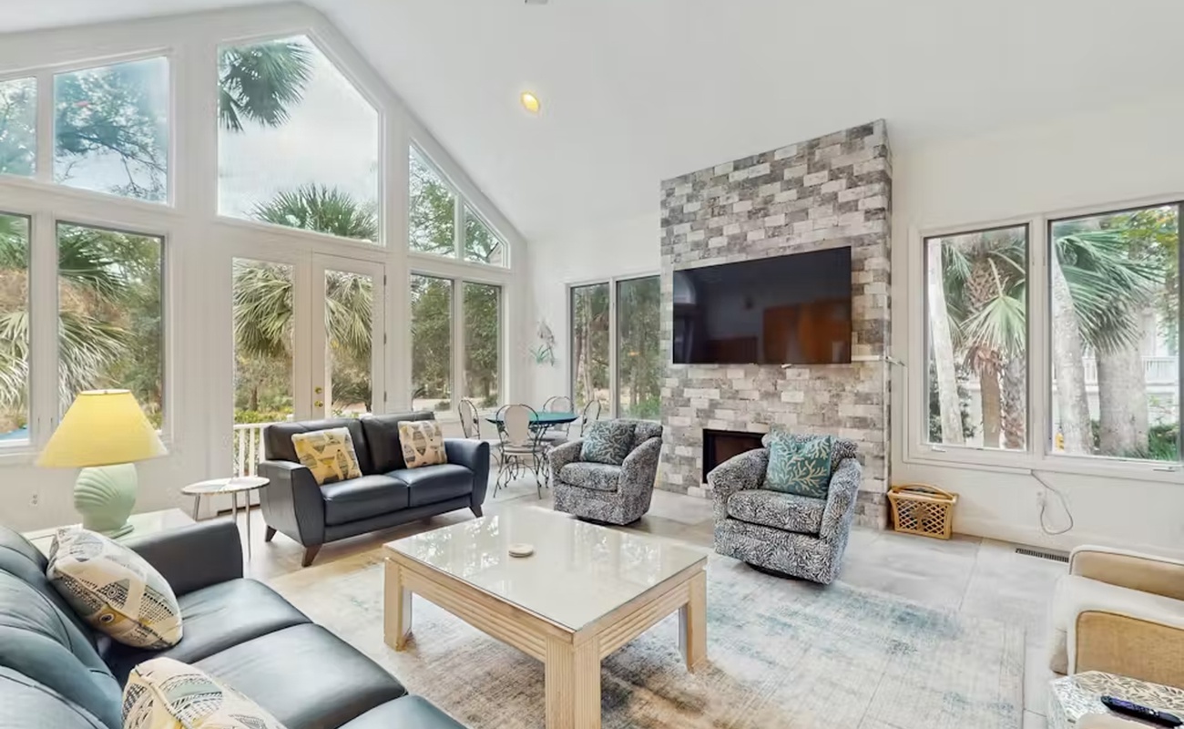 Relax in your bright, airy living room with soaring ceilings and stone fireplace, surrounded by tropical views through floor-to-ceiling windows.