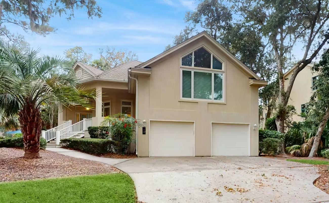 Charming two-story vacation home with tropical landscaping and two-car garage nestled among mature oak trees.
