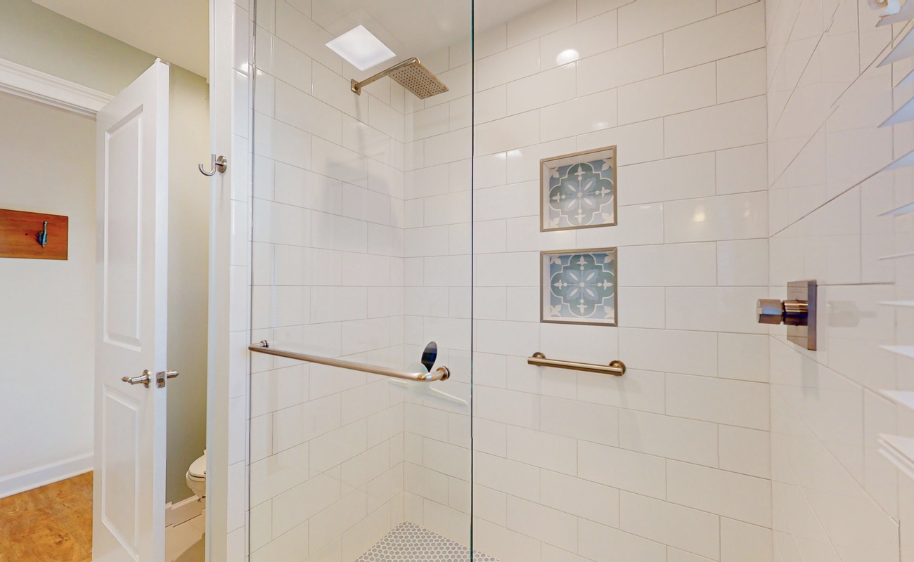 Step into your spacious walk-in shower with elegant tile work, gold fixtures, and thoughtful grab bars for your comfort and safety.