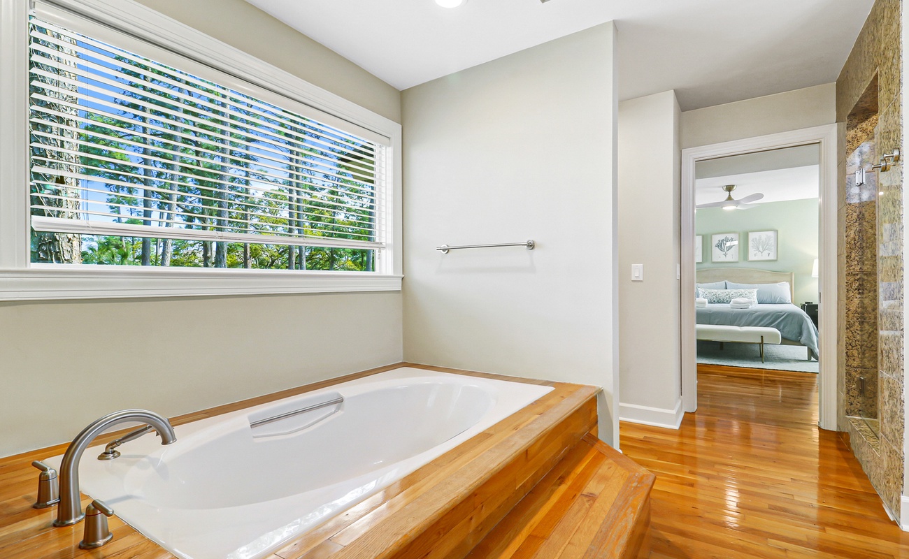 Unwind in your private spa-like bathroom featuring a deep soaking tub, polished hardwood floors, and leafy garden views.