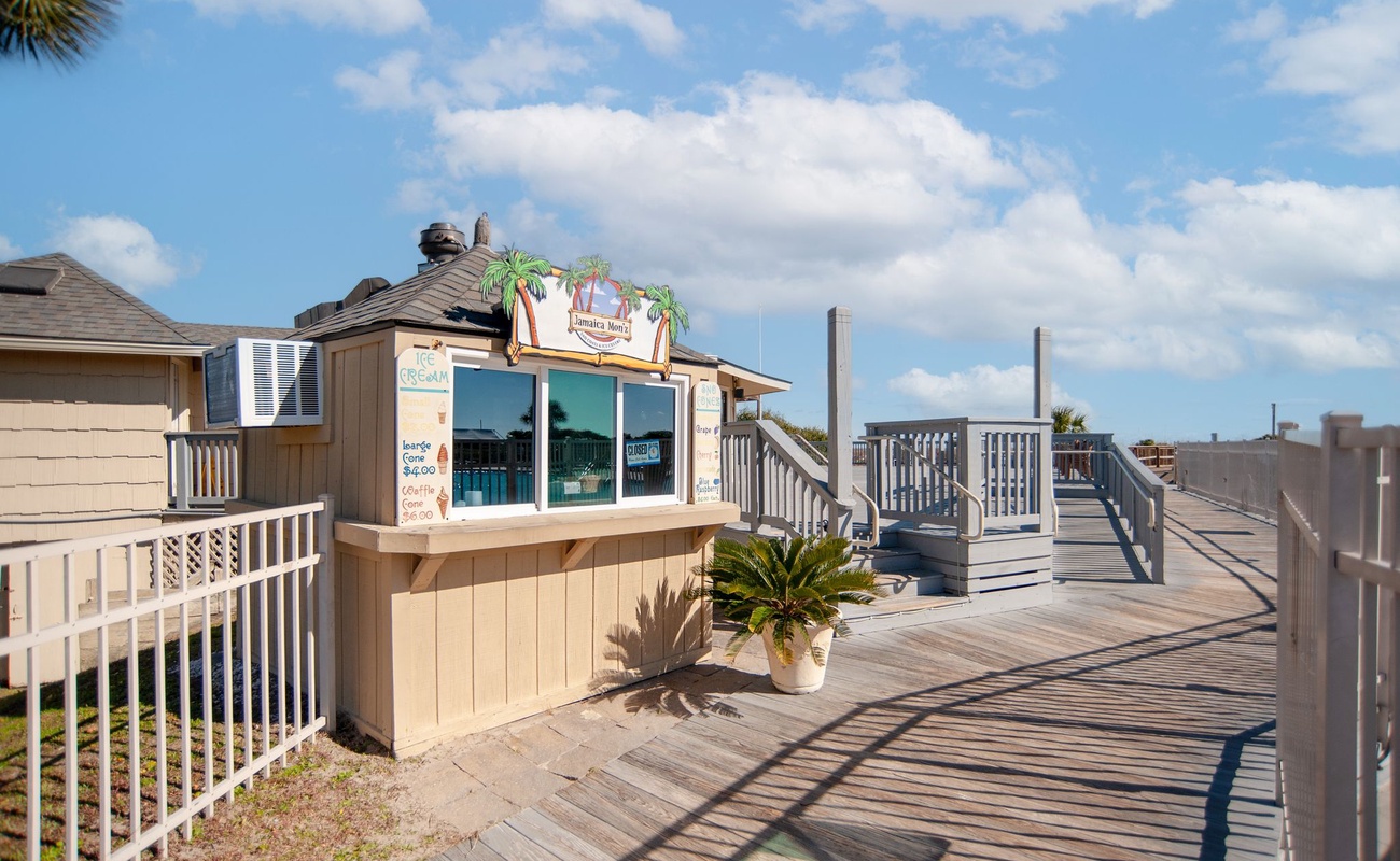 Beachside boardwalk leading to rental shop and beach access, surrounded by coastal homes and palm trees under sunny skies.