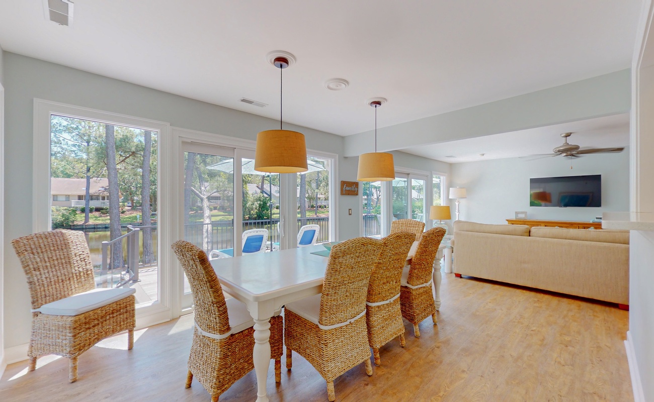 Natural light floods your dining space through expansive windows, where wicker chairs invite memorable meals with loved ones.