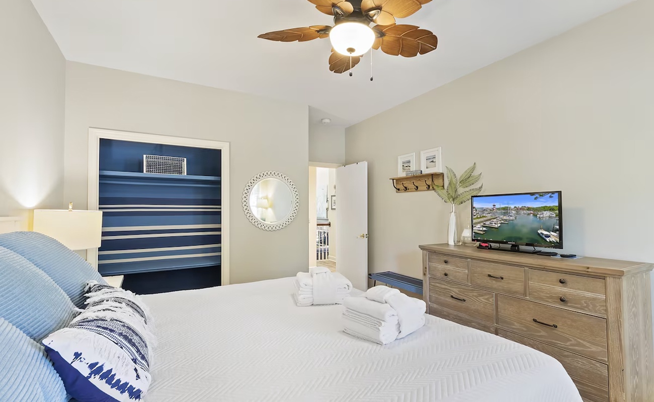 Unwind in your peaceful bedroom with coastal charm, featuring a plush bed, tropical ceiling fan, and entertainment center for perfect relaxation.